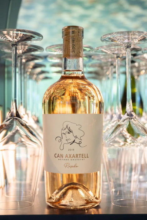 Geschlossene Flasche Roséwein "Rosado" von Can Axartell, Jahrgang 2019, zwischen zwei Weingläsern