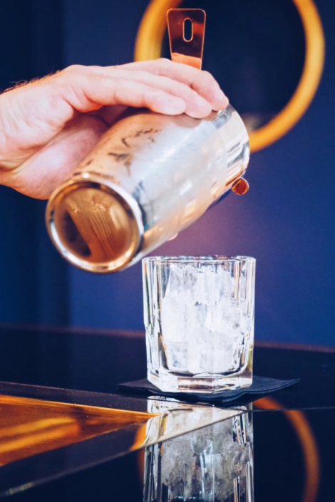 Ein Barkeeper gießt einen frisch zubereiteten Cocktail aus einem Shaker in ein Glas mit Eiswürfeln.